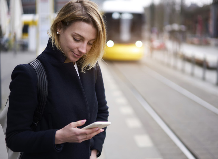 Lady stood on train platform whilst holding her unlock Metro phone handset.
